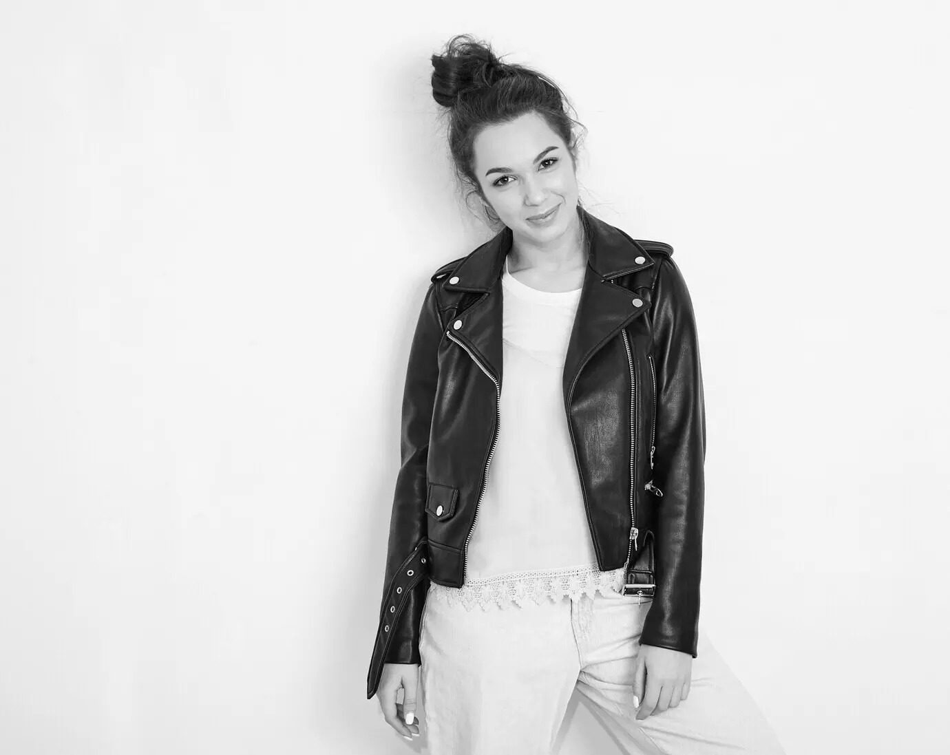 Porträt eines jungen, schönen, brünetten Mädchen-/Frauen-Models mit Nude-Make-up, das eine sommerliche Hipster-Biker-Lederjacke trägt und in der Nähe einer Wand posiert.